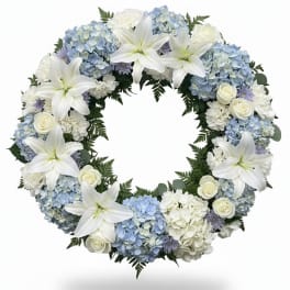 Circular wreath of white lilies, blue hydrangeas, and white roses