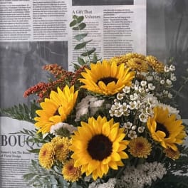 Bouquet of sunflowers, white filler flowers, and yellow mums in a white vase