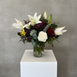 Mixed bouquet with white lilies, roses, and purple flowers in a glass vase