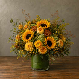 Sunflower and yellow flower arrangement in a green glass vase