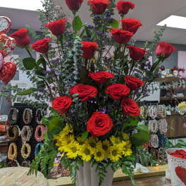 Tall arrangement of red roses and yellow daisies in a white vase