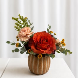 Orange rose and peach carnation arrangement in a brown vase