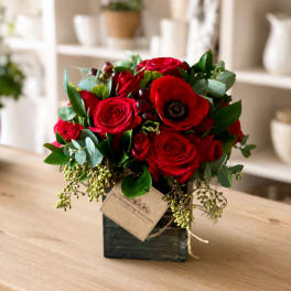 Red rose arrangement in a square vase with eucalyptus and a decorative tag