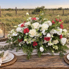 Large white and red floral centerpiece on a rustic table outdoors