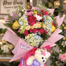 Mixed bouquet in pink wrap with a teddy bear attached at the base