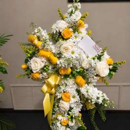 Cross-shaped floral spray with white and yellow flowers on a stand