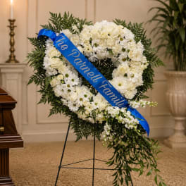 White funeral wreath with a blue memorial ribbon on a stand