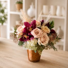 Bouquet of blush roses and deep magenta orchids in a copper vase