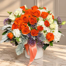 Orange and white rose bouquet in a ribbed vase with a peach ribbon