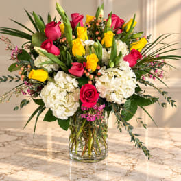 Bouquet of pink and yellow roses with white hydrangeas in a clear glass vase