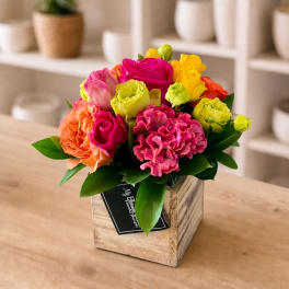 Bright mixed bouquet in a rustic wooden box with pink, yellow, and orange blooms