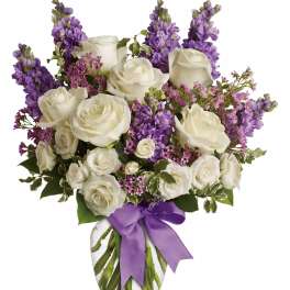 White roses and purple flowers in a glass vase with a purple ribbon
