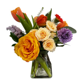Mixed bouquet of orange, yellow, cream, and purple flowers in a glass vase