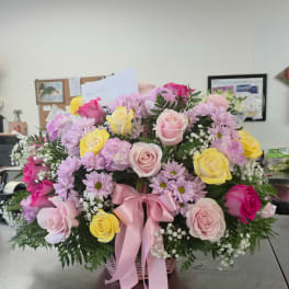 Mixed pink, yellow, and lavender flowers in a basket with a pink ribbon