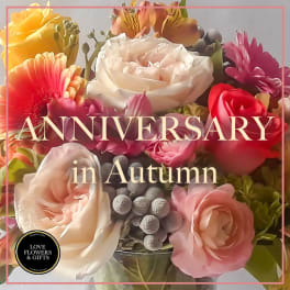 Mixed bouquet of peach and pink roses with bright accent flowers in a glass vase