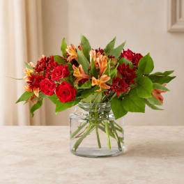 Red roses and orange flowers arranged in a clear glass vase