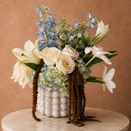 White roses and lilies with blue flowers in a white vase