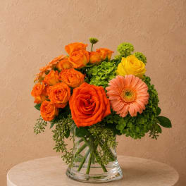Orange roses and a peach gerbera daisy in a clear glass vase