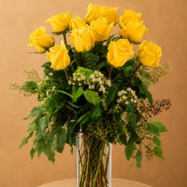 Yellow roses arranged in a clear glass vase with greenery
