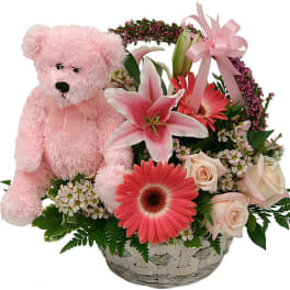 Pink teddy bear beside a basket of pink and white flowers