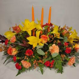 Low floral centerpiece with yellow lilies, orange roses, and orange candles