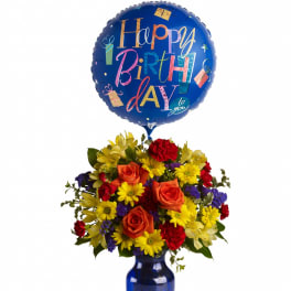 Bright birthday bouquet of orange roses and yellow daisies in a blue vase with a blue Happy Birthday balloon.
