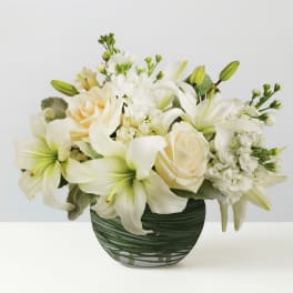 White lilies and roses arranged in a green glass vase