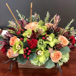 Peach roses and green orchids in a rectangular vase with red accents