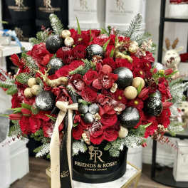 Red rose arrangement in a black hat box with gold ornaments and ribbon