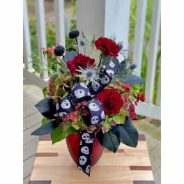 Red carnations and mixed blooms in a red vase with a skull-pattern ribbon
