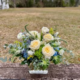 Cream roses and blue flowers arranged in a clear glass vase