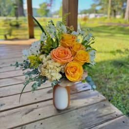 Yellow and peach roses arranged in a small vase with white filler flowers