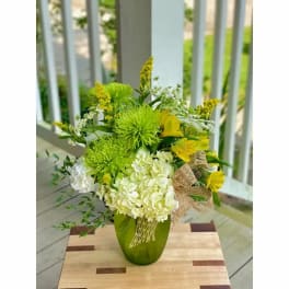 Green and white floral arrangement in a green vase with yellow accents