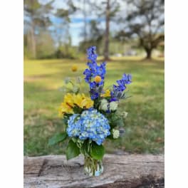 Blue and yellow mixed flower arrangement in a clear glass vase