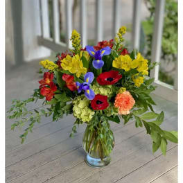 Mixed bouquet in a clear glass vase with red, yellow, blue, and peach flowers