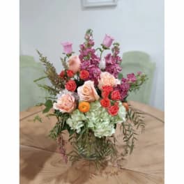 Mixed bouquet of pink, peach, and coral flowers in a clear glass vase