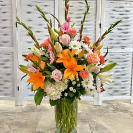 Tall mixed bouquet of orange lilies, pink roses, and white daisies in a glass vase