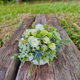 White and green floral arrangement in a low white bowl on weathered wood