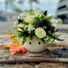 White rose arrangement in a small cream vase with a face design