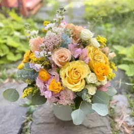 Mixed bouquet of yellow, peach, pink, and white flowers in a white vase