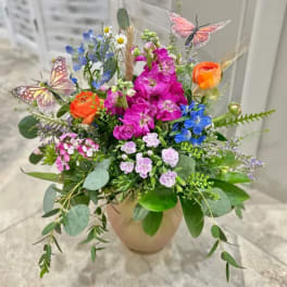 Mixed bouquet in a beige vase with orange, pink, blue, and lavender flowers
