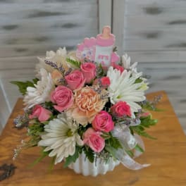 Pink roses and white daisies in a white vase with a baby-themed topper