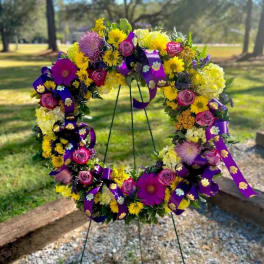 Circular floral wreath on a stand with purple ribbons and yellow, pink, and purple flowers