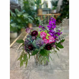Mixed bouquet of pink roses, purple blooms, and greenery in a glass vase