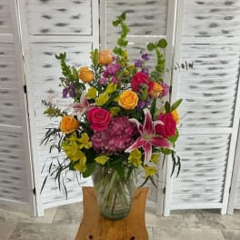 Mixed bouquet of roses, lilies, and purple blooms in a glass vase