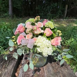 Pink roses and white hydrangeas arranged in a glass vase with ribbon.
