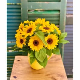 Yellow daisy-like flowers arranged in a yellow pitcher vase