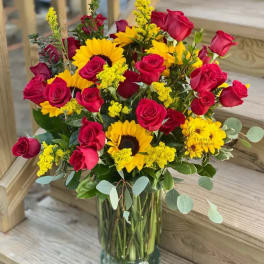 Bouquet of red roses and yellow sunflowers in a clear glass vase