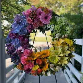 Colorful floral wreath on a black stand with roses, hydrangeas, and sunflowers