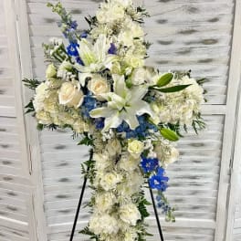 Large white floral cross arrangement with blue accents on a stand